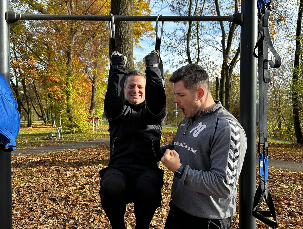 Personal Training outdoor – Coach feuert Klient beim Klimmzug an